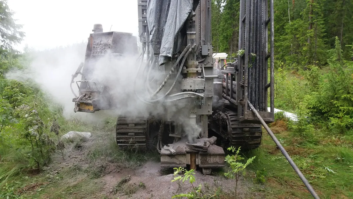 Porauslaite suorittaa maaperätutkimusta metsäisessä maastossa, ja porauksesta nousee runsaasti pölyä.